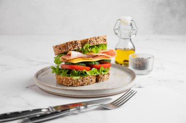 Jambonlu, peynirli, marullu, domatesli, salatalıklı ve mermer arkaplanlı bir tabakta ekmek. Lezzetli, hızlı ve sağlıklı bir kahvaltı. Ön görünüm, boşluğu kopyala.