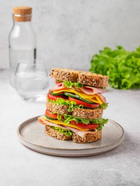 Jambonlu, peynirli, marullu ve sebzeli üçlü sandviç tabakta tam tahıllı ekmek ve bir bardak su ve taze salata. Kavram, taze ve sağlıklı bir atıştırmalıktır. Ön görünüm.