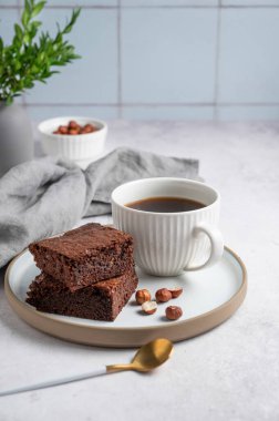 Tabakta çikolatalı kek parçaları ve arka planda fındıklı, kaşıklı, peçeteli ve çiçekli bir fincan espresso kahvesi. Kahvaltı için ev yapımı tatlı hamur işi kavramı. Ön görünüm, boşluğu kopyala.