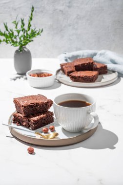 Tabakta çikolatalı kek parçaları ve mermer arka planda fındıklı, peçeteli, kaşıklı ve dallı bir fincan espresso kahvesi. Kahvaltı için ev yapımı tatlı hamur işi kavramı. Ön görünüm, boşluğu kopyala.