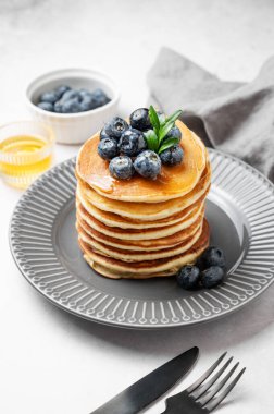 Taze yaban mersinli krep yığını ve bal, böğürtlen, peçete ve şirin bir kapakla arka planda gri bir tabakta suryp. Lezzetli ve besleyici bir kahvaltı ya da brunch konsepti. Ön görünüm, boşluğu kopyala.