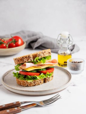 Jambonlu, peynirli, marullu, domatesli, salatalıklı ve mermer arka planda bir tabakta ekmek, çatal bıçak, baharat ve peçeteli. Lezzetli, hızlı ve sağlıklı bir kahvaltı. Ön görünüm, boşluğu kopyala.