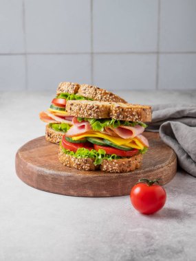 Salamlı, peynirli, marullu ve sebzeli iki sandviç beton zemin üzerinde tahta bir tahta üzerinde peçete ve domatesli. Sağlıklı, ev yapımı atıştırmalıklar. Ön görünüm, boşluğu kopyala.