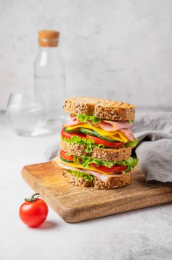 Jambonlu, peynirli, marullu ve sebzeli üçlü sandviç. Tahta üzerinde tahıllı ekmek ve bir bardak su ve peçeteyle. Taze ve sağlıklı atıştırmalık kavramı. Ön görünüm, boşluğu kopyala.