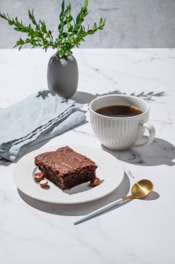 Tabakta çikolatalı kek parçaları ve mermer arka planda fındıklı, peçeteli, kaşıklı ve dallı bir fincan espresso kahvesi. Kahvaltı için ev yapımı tatlı hamur işi kavramı. Ön görünüm, boşluğu kopyala.