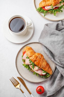 Jambonlu kruvasan sandviçi, mozarella peyniri, domates, bir tabak roka ve arka planda hafif arkaplanda bir fincan kahve. Sağlıklı bir kahvaltı ya da brunch kafe menüsü. Üst görünüm, alanı kopyala.