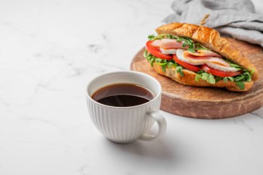 Jambonlu kruvasan sandviçi, mozarella peyniri, domates, ahşap bir tahtada roka ve mermer zemin üzerinde bir fincan kahve. Sağlıklı bir kahvaltı ya da brunch kafe menüsü. Ön görünüm, boşluğu kopyala.