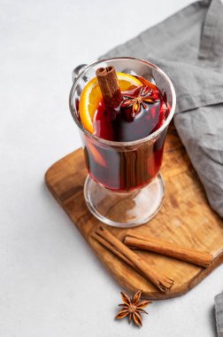 Bir bardak sıcak şarap, portakal, tarçın ve arka planda hafif bir arkaplanda, baharat ve peçeteli ahşap bir tahta üzerinde yıldız anason. Sıcak bir kış içeceği ve sıcak bir ev atmosferi. Üst görünüm, alanı kopyala.