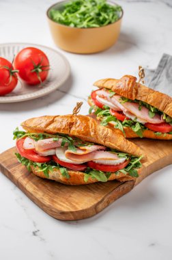 Jambonlu kruvasan sandviçi, mozarella peyniri ve mermer zemin üzerinde ahşap bir tahta üzerinde taze bitki ve domatesli roka. Sağlıklı kahvaltı ya da brunch kavramı. Ön görünüm.