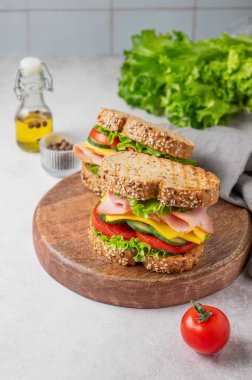 Baharatlı, salamlı, peynirli, marullu ve sebzeli iki sandviç, ahşap bir tahtada, baharatlı, taze salatalı ve peçeteli. Sağlıklı, ev yapımı atıştırmalıklar. Boşluğu kopyala.