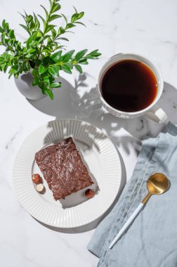 Tabakta çikolatalı browni ve mermer arka planda bir fincan espresso kahvesi yeşil dalı, peçetesi, kaşığı ve sabah gölgesi olan. Kahvaltı için ev yapımı tatlı hamur işi kavramı. Üst görünüm, alanı kopyala.