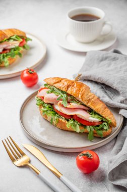 Jambonlu kruvasan sandviçi, mozzarella peyniri, domates, bir tabak roka ve arka planda hafif arkaplanda bir fincan kahve, içinde de Cutlry ve peçete. Sağlıklı bir kahvaltı ya da brunch kafe menüsü. Ön görünüm