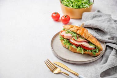 Jambonlu kruvasan sandviç, mozzarella peyniri ve hafif bir arka planda hafif bir tabakta roka, bitki ve çatal bıçaklı. Sağlıklı bir kahvaltı ya da branç menüsü için reklam pankartı konsepti. Ön görünüm, boşluğu kopyala