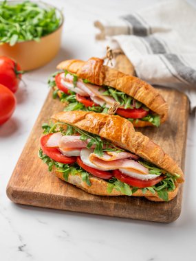 İki tane jambonlu kruvasan sandviç, mozzarella peyniri ve ahşap bir tahta üzerinde mermer bir arka planda otla birlikte roka. Sağlıklı bir kahvaltı ya da branç menüsü için reklam pankartı konsepti. Ön görünüm