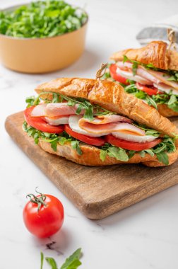 İki tane jambonlu kruvasan sandviç, mozzarella peyniri ve ahşap bir tahta üzerinde mermer bir arka planda otla birlikte roka. Sağlıklı kahvaltı ya da brunch kavramı. Ön görünüm.