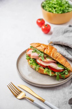 Jambonlu kruvasan sandviç, mozzarella peyniri ve hafif bir arka planda hafif bir tabakta roka, bitki ve çatal bıçaklı. Sağlıklı bir kahvaltı ya da branç menüsü için reklam pankartı konsepti. Ön görünüm, boşluğu kopyala