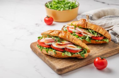 İki tane jambonlu kruvasan sandviç, mozzarella peyniri ve ahşap bir tahta üzerinde mermer bir arka planda otla birlikte roka. Sağlıklı kahvaltı ya da brunch kavramı. Ön görünüm, boşluğu kopyala.