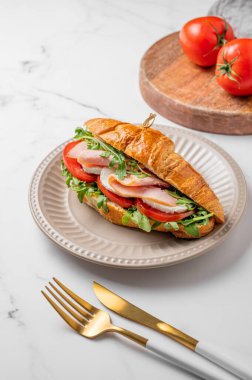 Jambonlu kruvasan sandviç, mozzarella peyniri ve mermer bir arka planda taze domates ve çatal bıçaklı roka. Sağlıklı kahvaltı ya da brunch kavramı. Boşluğu kopyala.