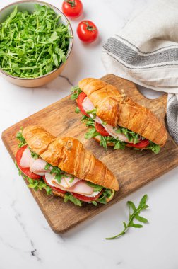 Jambonlu kruvasan sandviçi, mozzarella peyniri ve mermer arka planda ahşap bir tahta üzerinde taze bitki ve peçeteyle birlikte roka. Sağlıklı kahvaltı ya da brunch kavramı. Üst görünüm, alanı kopyala.