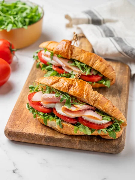 İki tane jambonlu kruvasan sandviç, mozzarella peyniri ve ahşap bir tahta üzerinde mermer bir arka planda otla birlikte roka. Sağlıklı bir kahvaltı ya da branç menüsü için reklam pankartı konsepti. Ön görünüm