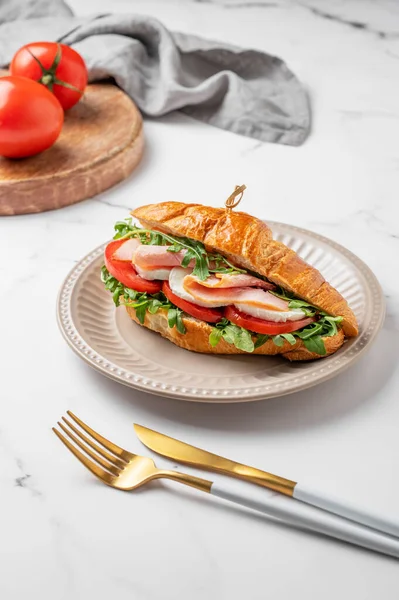 Jambonlu kruvasan sandviç, mozzarella peyniri ve mermer bir arka planda taze domates ve çatal bıçaklı roka. Sağlıklı kahvaltı ya da brunch kavramı. Ön görünüm, boşluğu kopyala.