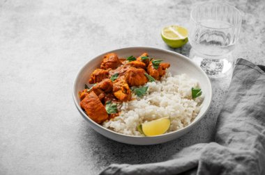 Beton zemin üzerinde basmati pilavlı Hint tereyağlı tavuk körisi, bir bardak su, peçete ve limon. Restoranın reklam menüsü için geleneksel, otantik doğu yemekleri konsepti. Ön görünüm, boşluğu kopyala.