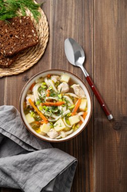 Koyu ahşap arka planda, kepekli ekmek, peçete ve kaşıkla taze dereotlu tavuk çorbası. Köy tarzında sağlıklı ev yemeği kavramı. Üst görünüm, alanı kopyala.