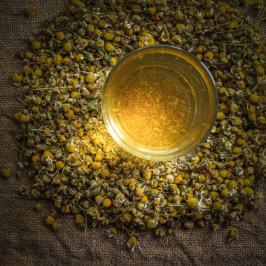 Masada bir bardak papatya çayı. Bir ışık huzmesi ile üstten görünüm. 