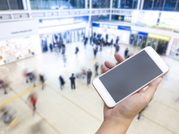 Hand holding smart phone with passengers inside transit station 