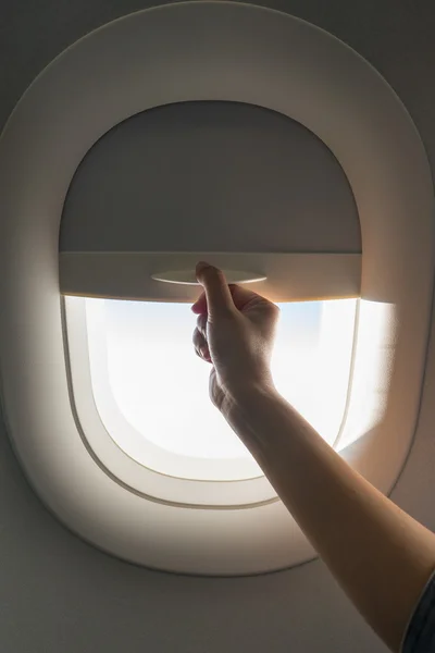 Hand pulling down aircraft window curtain — Stock Photo, Image