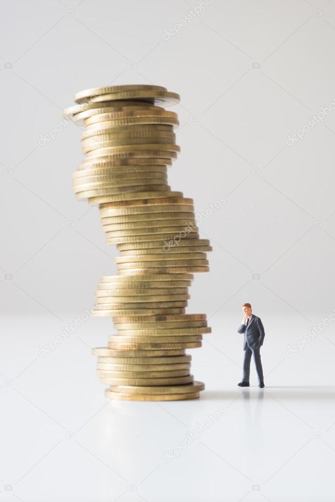 Businessman standing on risky coin stack. 