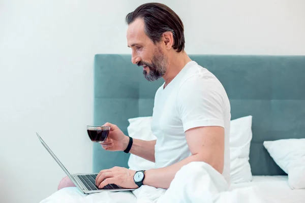 Positivo Homem Confiante Sentado Cama Sob Cobertor Usando Laptop Moderno — Fotografia de Stock