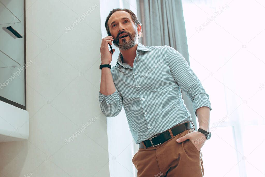 Attentive young man being involved in a phone conversation while standing near the wall at home