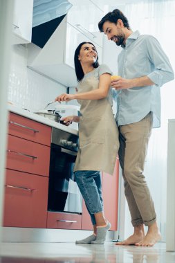 Önlük giymiş neşeli bir kadın çorba karıştırıyor ve yanında bir bardak meyve suyu olan bir adama dönüyor.