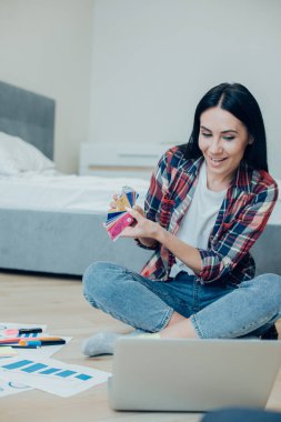 Pozitif genç bayan, gündelik giysiler içinde yerde oturuyor ve dizüstü bilgisayarının web kamerasında renk paletleri gösteriyor.