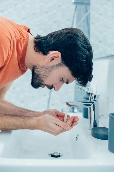 若い暗い髪の男の肖像シンクに向かって傾いて実行中の水に手を入れて — ストック写真