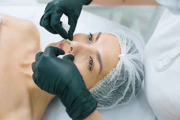 Face of a calm Caucasian woman and hands of beautician removing dirt with cotton pads