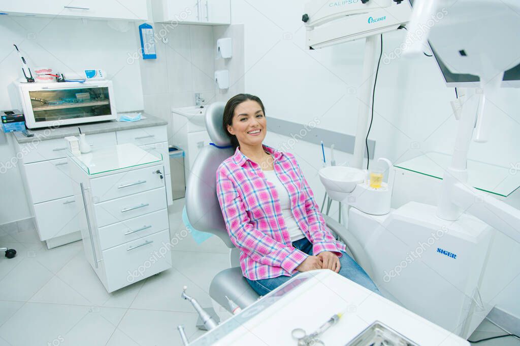 Mirthful Caucasian woman in casual clothes sitting in a dental chair of a modern office and smiling