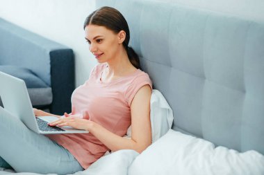 Yoğunlaşmış bir kadın bilgisayarın ekranına bakıyor ve yatakta otururken dokunmatik ped kullanıyor.