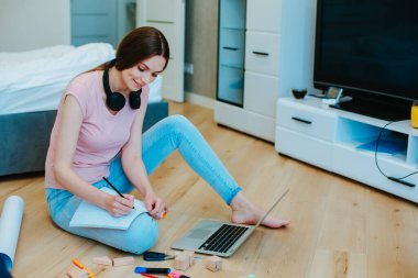Fotokopi kitabının bir sayfasına yazı yazan Gladsome lady dizüstü bilgisayarın önünde yerde otururken