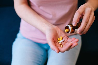 Tanınmayan bir kadın elinde küçük bir cam şişeyle ondan haplar alıyor.