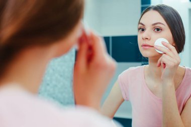 Güzel bir genç bayanın portresi aynada yüzüne bakarken pamukla temizliyor.