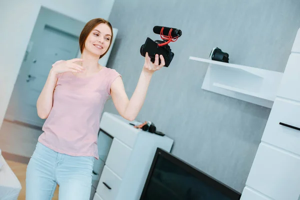 Happy young lady in casual clothes standing with a camera and microphone and smiling