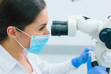Mikroskop gözünden bakan maske takan kadın bir sağlık görevlisine yaklaş.