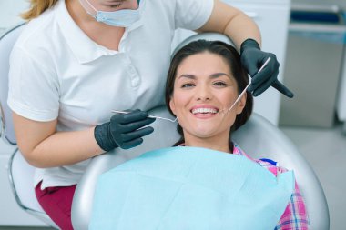 Beyaz bir kadının elinde diş aynası olan bir doktorla diş muayenesi yaptırmasının mutlu bir gülümsemesi.