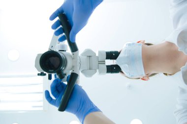 Modern bir diş mikroskobu kullanarak tıbbi maske takan bir tıp çalışanının alt görüntüsü.