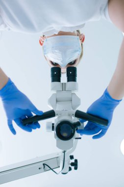 Diş mikroskobuyla göz çukuruna bakan bir kadın sağlık görevlisinin alt görüntüsü.