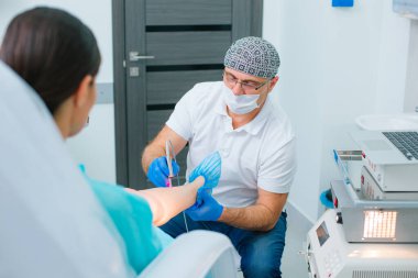 Klinikteki hastasının bacağındaki küçük damarları tedavi etmek için lazer kullanmakta usta bir dermatolog.