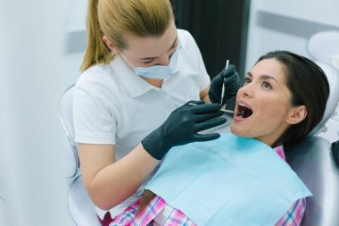 Dikkat et, profesyonel dişçi maske ve eldivenle hastasının dişlerine bakıyor.