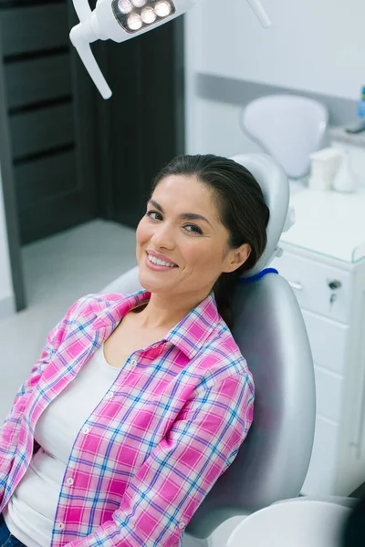 Contented woman in casual clothes sitting in a medical chair of a dental clinic and smiling